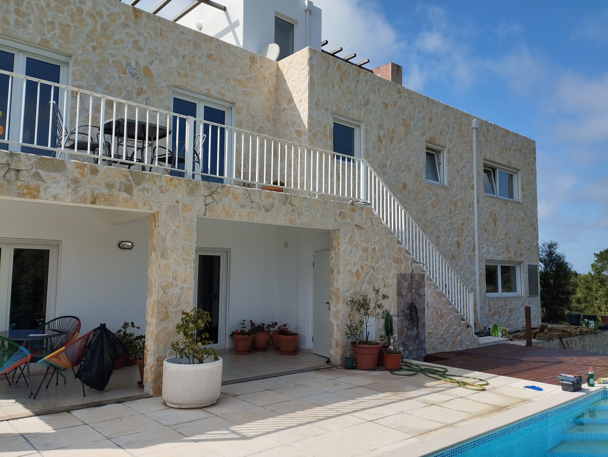 Finished stone-clad Silver Coast villa by Michael Sterrenberg — full exterior cladding, pool surround, white railed balcony staircase, showcasing the family's stonework on the Silver Coast