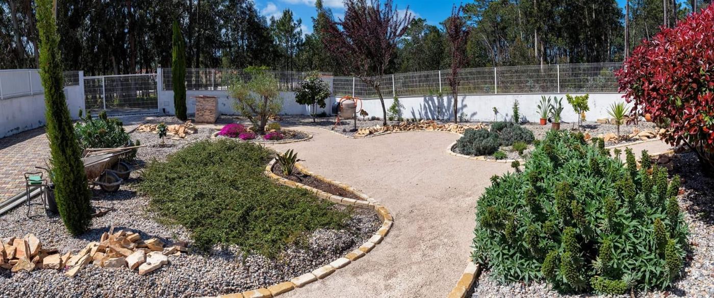 A wide panoramic view of a finished landscaped garden with rounded stone-edged paths, mixed planting beds and a fenced perimeter on the Silver Coast