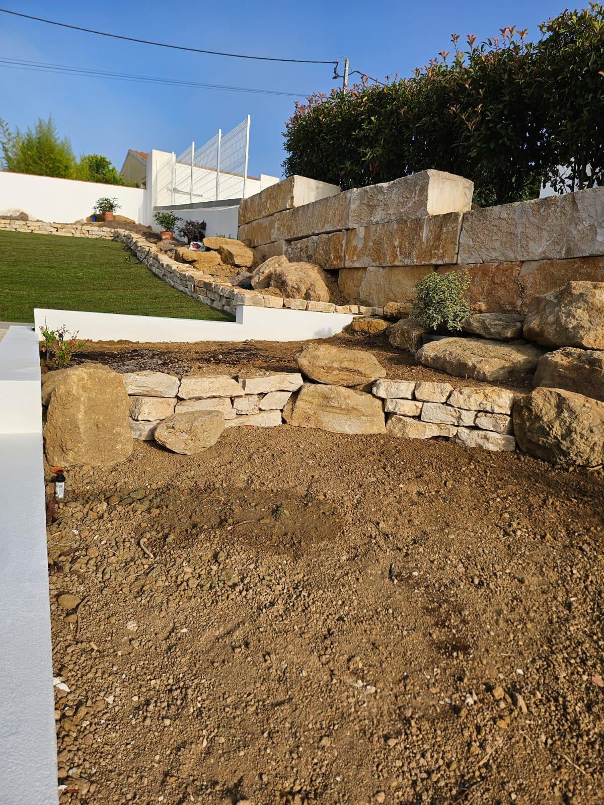 A hand-laid natural stone retaining wall in tiered sections holding back a manicured Silver Coast garden, built by Michael Straub