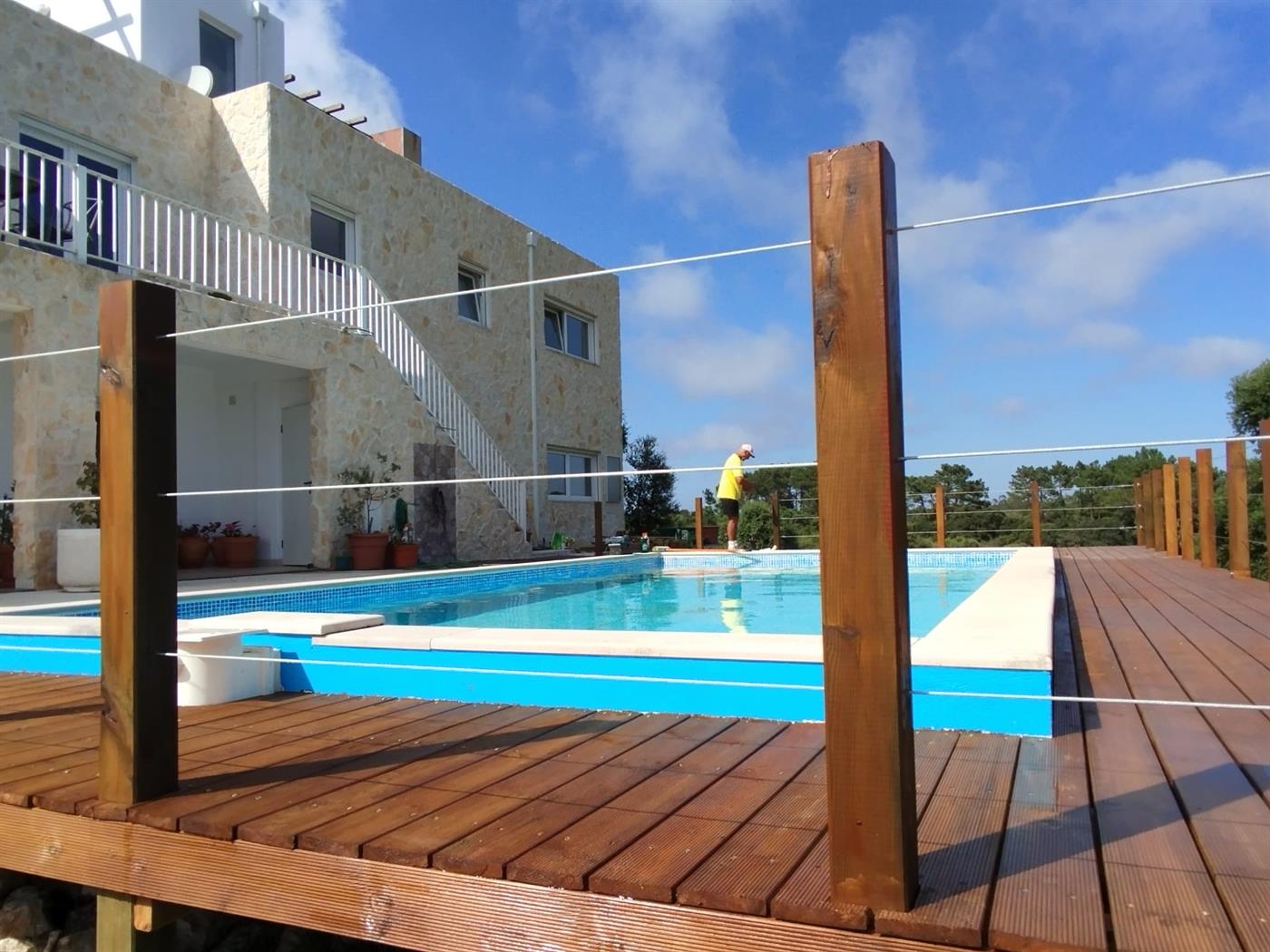 A Silver Coast villa with full natural-stone cladding, hardwood deck wrapping around an infinity pool and glass-cable safety railing, built by Michael Straub